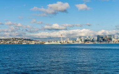Seattle siluetinin mimarisi. Önünde Elliott Körfezi, üstünde bulutlar var. Sahnede bir feribot da var..