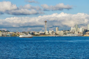 Seattle siluetinin mimarisi. Önünde Elliott Körfezi, üstünde bulutlar var. Olay yerinde bir su taksisi de var..