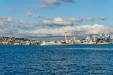 Seattle siluetinin mimarisi. Önünde Elliott Körfezi, üstünde bulutlar var. Sahnede bir feribot da var..