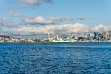 Seattle siluetinin mimarisi. Önünde Elliott Körfezi, üstünde bulutlar var. Sahnede bir feribot da var..
