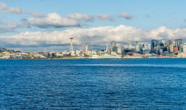 Seattle siluetinin mimarisi. Önünde Elliott Körfezi, üstünde bulutlar var. Sahnede bir feribot da var..