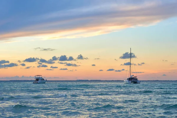 2 yachts at sunset on north beach isla mujeres. shades of blue and orange in the sky full of clouds. riviera maya beaches.
