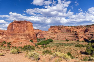 Arizona 'daki Chelly Ulusal Anıtı Kanyonu' ndaki kırmızı kaya oluşumlarının ve yemyeşil yeşilliğin güzel manzarası. Açık mavi gökyüzü ve kabarık bulutlar nefes kesici manzarayı güçlendirir..