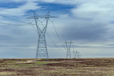 Yüksek voltajlı elektrik hatları, bulutlu bir gökyüzünün altında kırsal bir kırsal alana yayılıyor. Enerji iletimi ve altyapı kavramı.