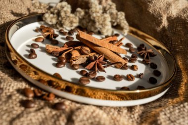 Altın bir tabakta tarçın ve anason, kahve çekirdekleri ve çuval bezi. Sert doku ve baharat kompozisyonu. Kurumuş çiçeklerle. Şekerleme, fırın ve Noel kartlarında kullanılıyor.