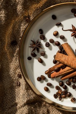 Altın bir tabakta tarçın ve anason, kahve çekirdekleri ve çuval bezi. Sert doku ve baharat kompozisyonu. Kurumuş çiçeklerle. Şekerleme, fırın ve Noel kartlarında kullanılıyor.