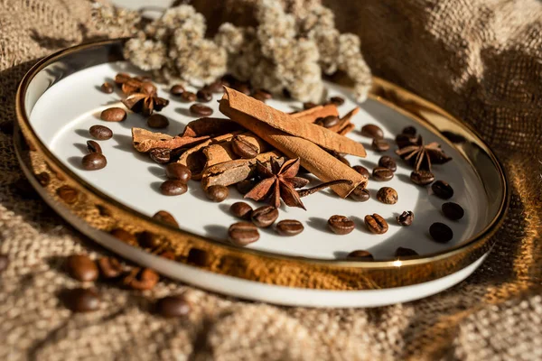 Altın bir tabakta tarçın ve anason, kahve çekirdekleri ve çuval bezi. Sert doku ve baharat kompozisyonu. Kurumuş çiçeklerle. Şekerleme, fırın ve Noel kartlarında kullanılıyor.