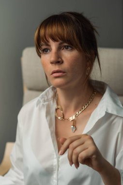 Beyaz gömlekli, çilli beyaz bir kadın. Estetik fotoğraf, sakin duygular, sandalyede oturmak.