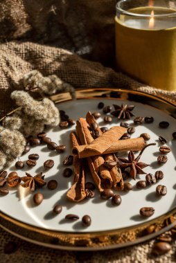 Mumların zarif bir kompozisyonu, baharatların bulunduğu altın kenarlı tabaklar - anason, tarçın ve kahve çekirdekleri. Çuval bezinin arka planına karşı