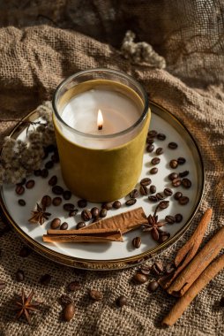 Mumların zarif bir kompozisyonu, baharatların bulunduğu altın kenarlı tabaklar - anason, tarçın ve kahve çekirdekleri. Çuval bezinin arka planına karşı