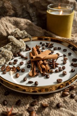 Mumların zarif bir kompozisyonu, baharatların bulunduğu altın kenarlı tabaklar - anason, tarçın ve kahve çekirdekleri. Çuval bezinin arka planına karşı