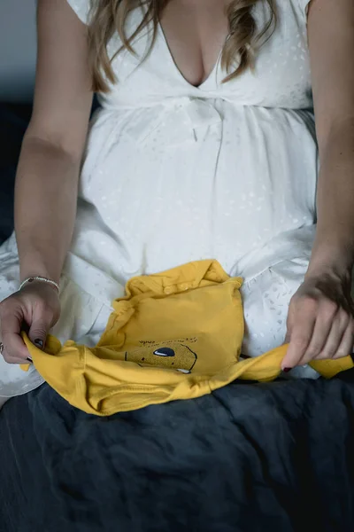 Έγκυος Λευκή Γυναίκα Λευκό Φόρεμα Διπλώνει Κίτρινα Βρεφικά Ρούχα — Φωτογραφία Αρχείου