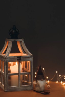 Güzel bir cüce, uzun şapkalı, kayak takımında ve kahverengi arka planda, mum, koni ve çelenkle süslenmiş. Kartpostallara ve Noel kutlamalarına uygun.