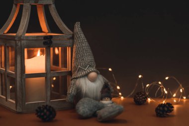 Uzun şapkalı sevimli bir cüce ve kahverengi arka planda bir kardan adam, mum, koni ve çelenkle süslenmiş. Kartpostallara ve Noel kutlamalarına uygun.