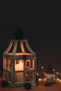 Güzel bir cüce, uzun şapkalı, kayak takımında ve kahverengi arka planda, mum, koni ve çelenkle süslenmiş. Kartpostallara ve Noel kutlamalarına uygun.