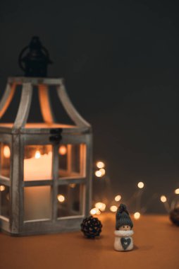 Kahverengi arka planda, mum, koni ve çelenkle süslenmiş sevimli bir kardan adam. Kartpostallara ve Noel kutlamalarına uygun.