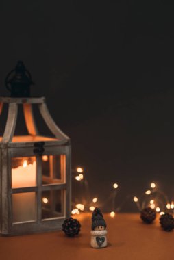 Kahverengi arka planda, mum, koni ve çelenkle süslenmiş sevimli bir kardan adam. Kartpostallara ve Noel kutlamalarına uygun.