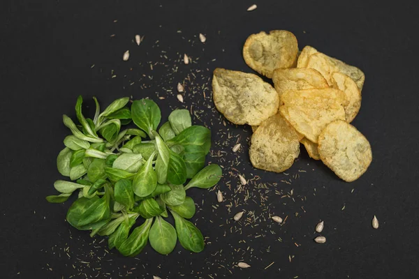 Lettuce leaves and chips on a black background. Healthy and unhealthy food is a contrast. Health care - the right choice of products