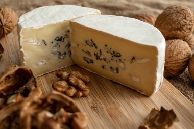 Çuval bezi arka planında bambu tahtasında beyaz ve yeşil küflü ve cevizli kesilmiş peynir kafasının bileşimi