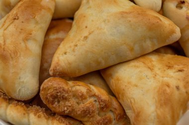 Altın kabuklu, üçgen şekilli ve at kuyruklu taze pişmiş turtalar ve çörekler.