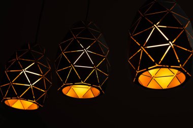 Geometrik desenli siyah lambalar, siyah zemin üzerinde üç lamba, sıcak ışıkla yanan, grafik desenli