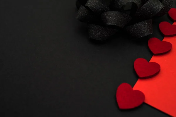 Black and red background, divided diagonally, decorated with a black bow and red hearts