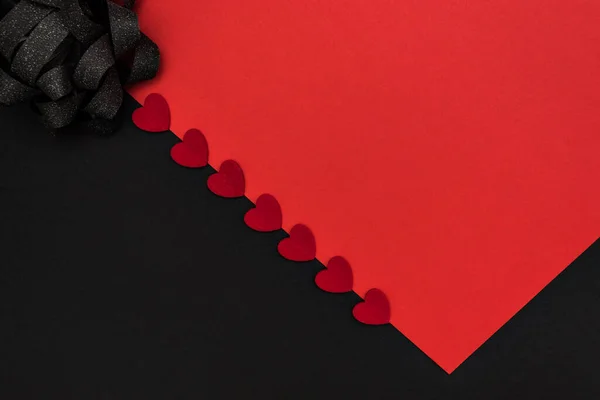 Black and red background, divided diagonally, decorated with a black bow and red hearts