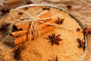 A bunch of cinnamon sticks, on cane sugar, with anise stars. Against the background of burlap.