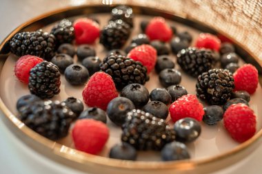 Raspberries and blackberries on a platter with a golden border. Healthy food on a plate.