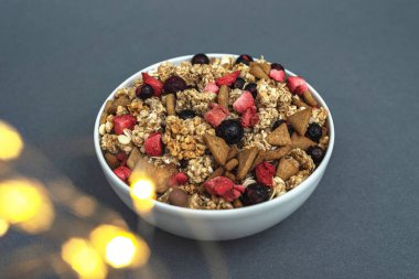 A bowl of muesli on a gray monochrome background, healthy food, healthy breakfast. With the glare of lights from the garland