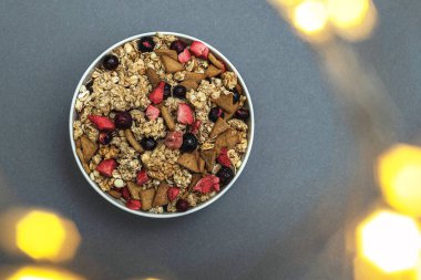 A bowl of muesli on a gray monochrome background, healthy food, healthy breakfast. With the glare of lights from the garland