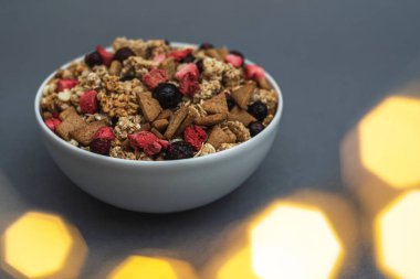 A bowl of muesli on a gray monochrome background, healthy food, healthy breakfast. With the glare of lights from the garland