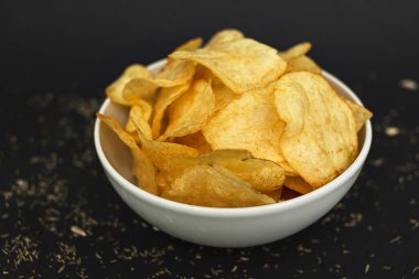 White ceramic bowl with golden potato chips on a black background.