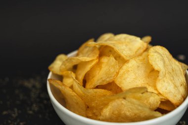 White ceramic bowl with golden potato chips on a black background.
