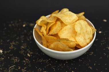 White ceramic bowl with golden potato chips on a black background.