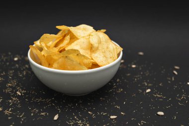White ceramic bowl with golden potato chips on a black background.