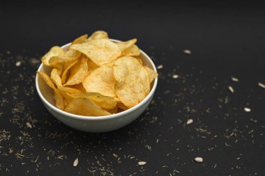 White ceramic bowl with golden potato chips on a black background.