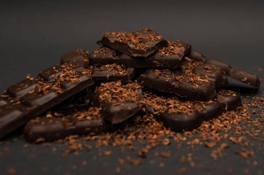 Pieces of dark and milk chocolate sprinkled with chocolate chips, on a dark background, close-up