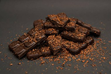 Pieces of dark and milk chocolate sprinkled with chocolate chips, on a dark background, close-up
