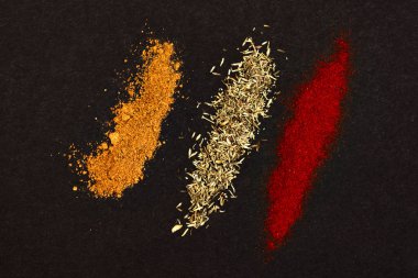 Spices scattered on a black background. Coriander, paprika and rosemary heaped on a dark background.