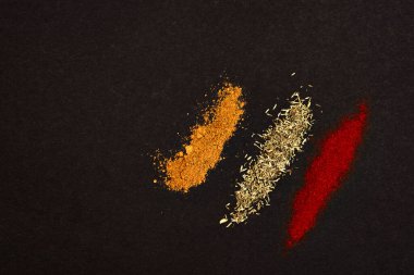 Spices scattered on a black background. Coriander, paprika and rosemary heaped on a dark background.