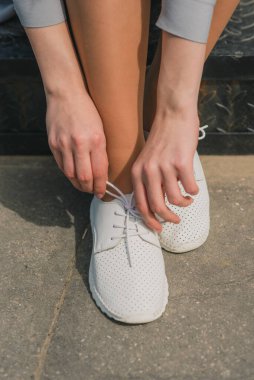 Sokakta ayakkabı bağcıklarını bağlayan genç kadın elleri.