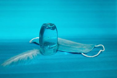 Mavi cep antiseptik jeli plastik şişe ve mavi arka planda koruyucu bir tıbbi maske. 