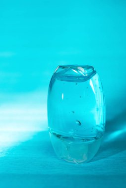 Cep antiseptik el dezenfektanı jeli mavi arka planda, etiketsiz. Küçük bir şişe şeffaf mavi antibakteriyel sıvı oksijen kabarcıkları, yuvarlak granüller. Su alkoliği, etil alkol.. 