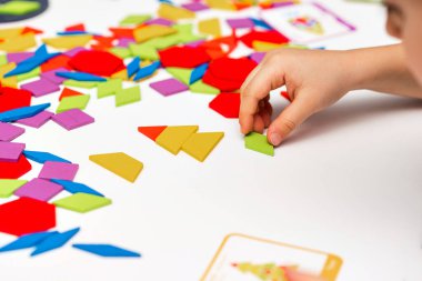 Parlak ahşap tangram oyuncağı oynayan çocuk elleri yakın plan. Çocuk ahşap parmaklık desenleri topluyor. Yaratıcı bebek yeni formlar yapar.