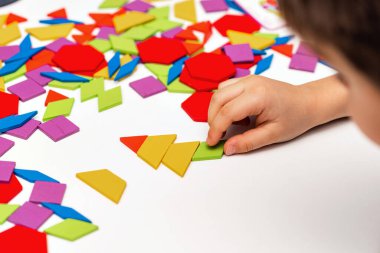 Parlak ahşap tangram oyuncağı oynayan çocuk elleri yakın plan. Çocuk ahşap parmaklık desenleri topluyor. Yaratıcı bebek yeni formlar yapar.
