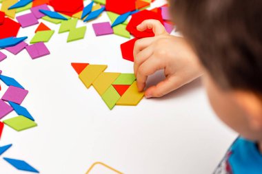 Parlak ahşap tangram oyuncağı oynayan çocuk elleri yakın plan. Çocuk ahşap parmaklık desenleri topluyor. Yaratıcı bebek yeni formlar yapar.