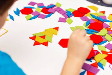 Parlak ahşap tangram oyuncağı oynayan çocuk elleri yakın plan. Çocuk ahşap parmaklık desenleri topluyor. Yaratıcı bebek yeni formlar yapar.