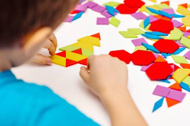 Parlak ahşap tangram oyuncağı oynayan çocuk elleri yakın plan. Çocuk ahşap parmaklık desenleri topluyor. Yaratıcı bebek yeni formlar yapar.