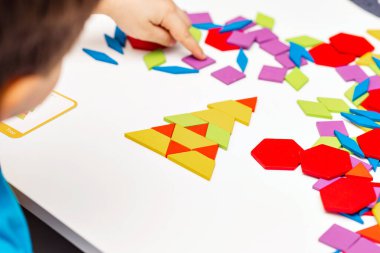 Parlak ahşap tangram oyuncağı oynayan çocuk elleri yakın plan. Çocuk ahşap parmaklık desenleri topluyor. Yaratıcı bebek yeni formlar yapar.